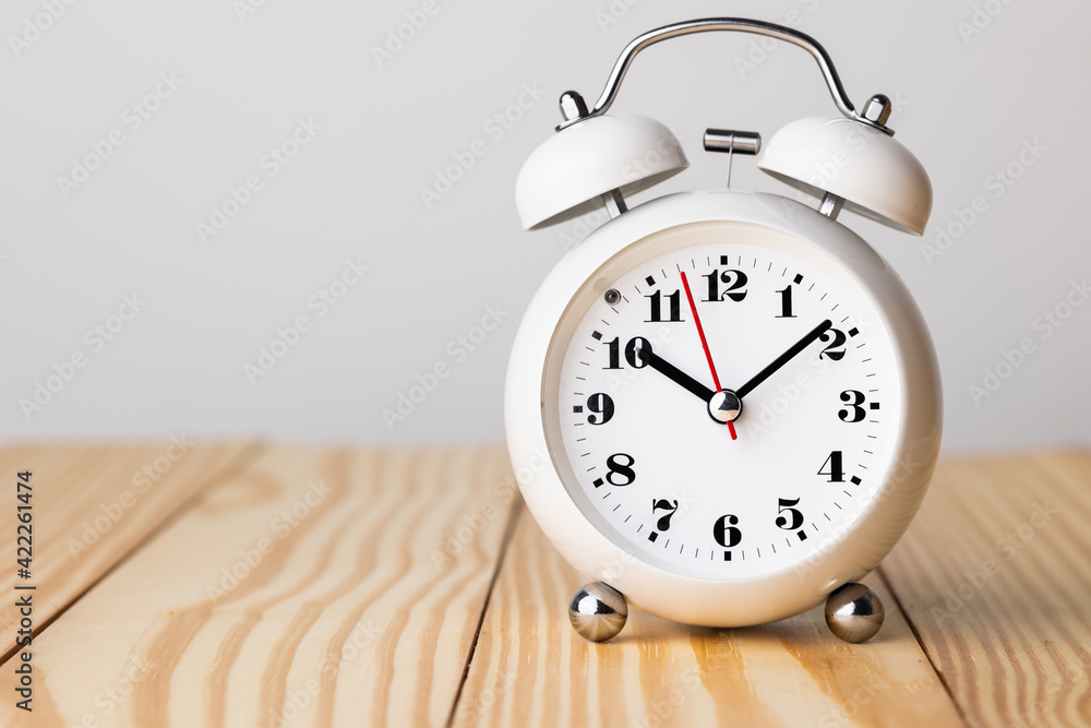 Small white alarm clock, black numbers, set the time for 10.10 o'clock, placed on a wood table. Small white alarm clock, black numbers, set the time for 10.10 o'clock, placed on a wood table.