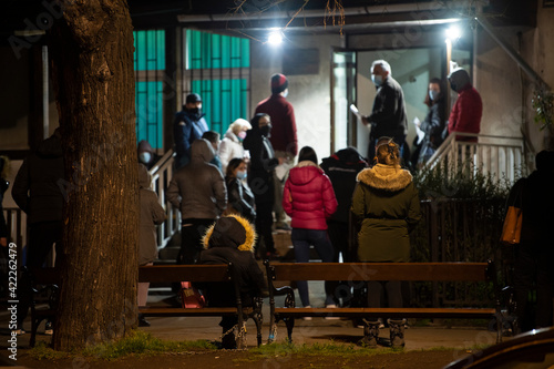 People stand in long queues on cold night in front of the checkpoint as they wait to receive the vaccine against corona virus - covid 19 or do PCR test. Mass vaccination. Belgrade, Serbia 20.03.2021