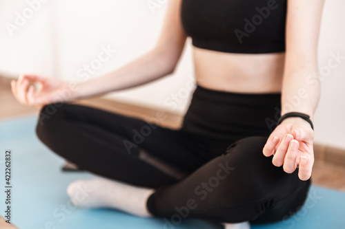 Close-up of the hands of a girl sitting on a yoga mat in a tracksuit and meditating in the lotus position. Faceless, young woman. Concentration, relaxation, mental health at home.