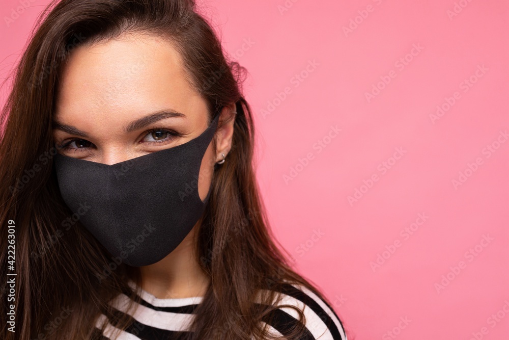 Woman wearing stylish protective face mask, posing on pink background. Trendy fashion accessory during quarantine of coronavirus pandemic. Close up studio portrait. Copy, empty space for text Woman wearing stylish protective face mask, posing on pink background. Trendy fashion accessory during quarantine of coronavirus pandemic. Close up studio portrait. Copy, empty space for text