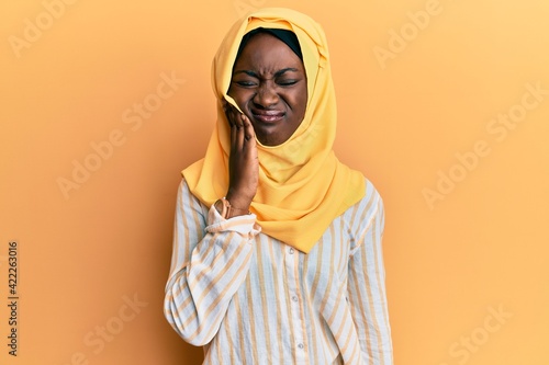 Beautiful african young woman wearing traditional islamic hijab scarf touching mouth with hand with painful expression because of toothache or dental illness on teeth. dentist © Krakenimages.com