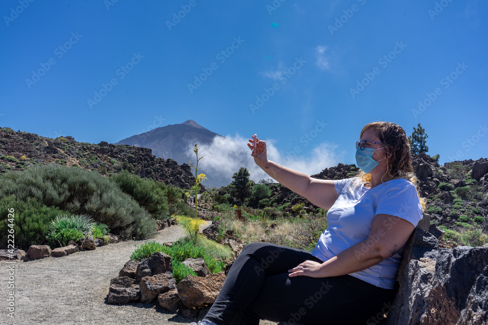 Young tourist woman with mask taking a selfie. In the background you can see Mount Teide, with its 3,178 meters high. This volcano is located in Tenerife, Canary Islands