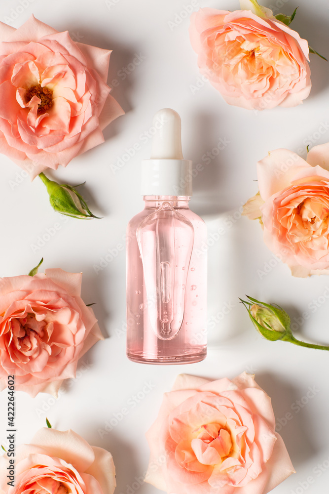 Bottles of serum with rose flowers flat lay on white background, copy space, top view Bottles of serum with rose flowers flat lay on white background, copy space, top view