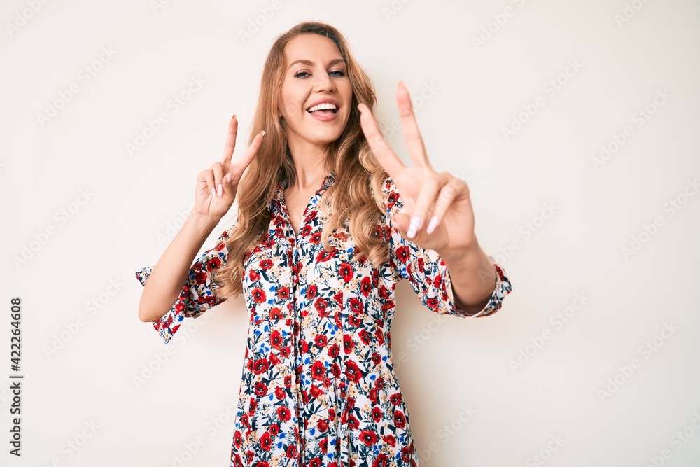 Young caucasian woman with blond hair wearing summer dress smiling looking to the camera showing fingers doing victory sign. number two. Young caucasian woman with blond hair wearing summer dress smiling looking to the camera showing fingers doing victory sign. number two.