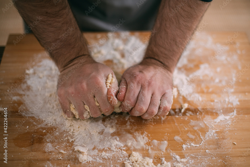 A male chef prepares noodle dough at home in the kitchen. Close up of hands with flour and dough