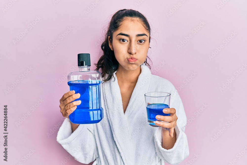 Hispanic teenager girl with dental braces holding mouthwash puffing cheeks with funny face. mouth inflated with air, catching air. Hispanic teenager girl with dental braces holding mouthwash puffing cheeks with funny face. mouth inflated with air, catching air.