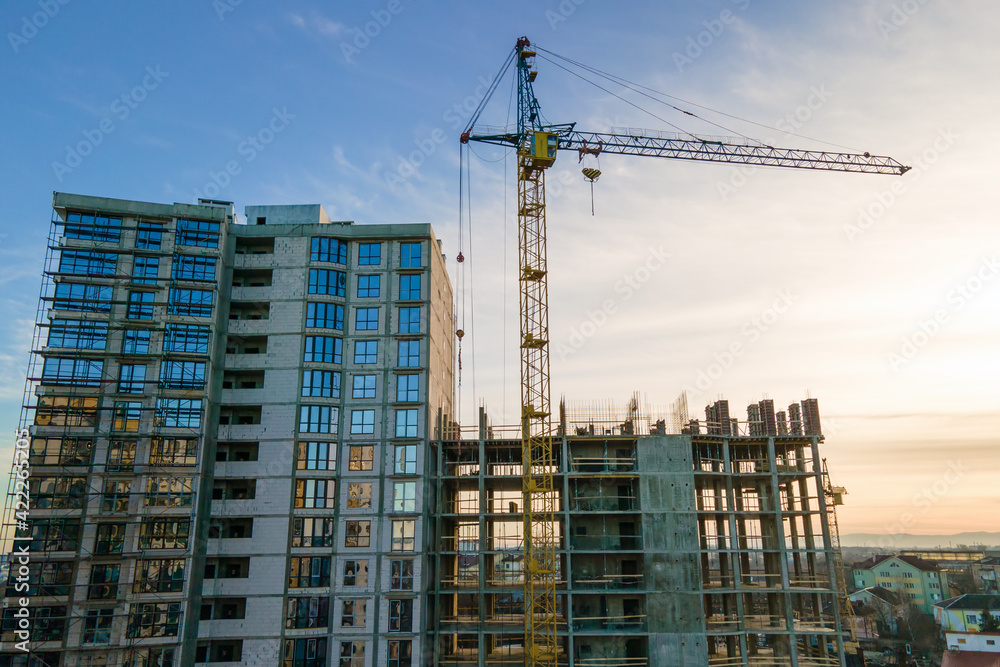 Aerial view of high tower crane and residential apartment building under construction at sunset. Real estate development.