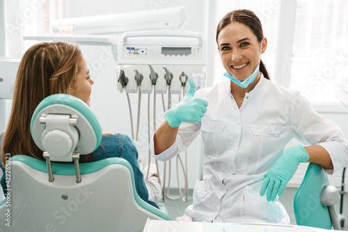 European mid dentist woman showing thumb up while working with patient