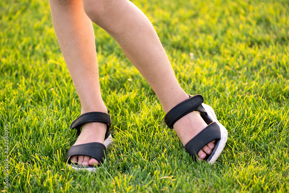 Closeup of young child girl legs standing on green grass lawn on warm summer evening.