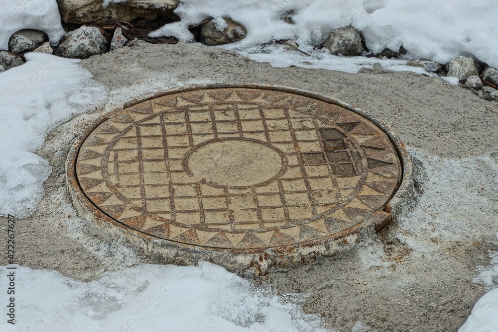 one rusty iron manhole on gray concrete in a snowdrift of white snow one rusty iron manhole on gray concrete in a snowdrift of white snow
