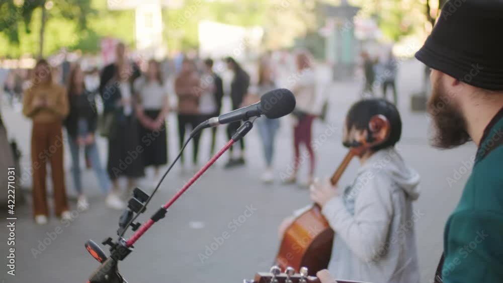Handheld shot of male street musician performing song for passerbys gathered around them on street