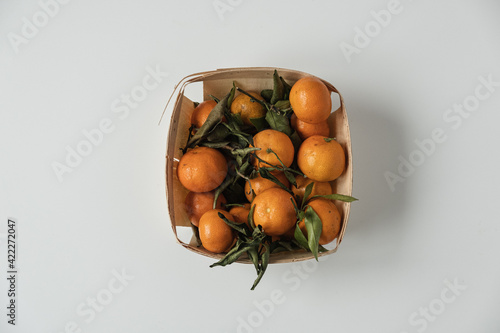Raw oranges  tangerines with green leaves in basket on white background. Fresh healthy fruits  food background. Flatlay  top view.