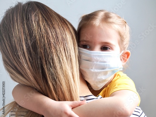 Children and mother wearing mask protect covid-19. Little girl daughter hugging mother on home background. Child wearing face mask, protect from infection of virus, pandemic, epidemic on quarantine