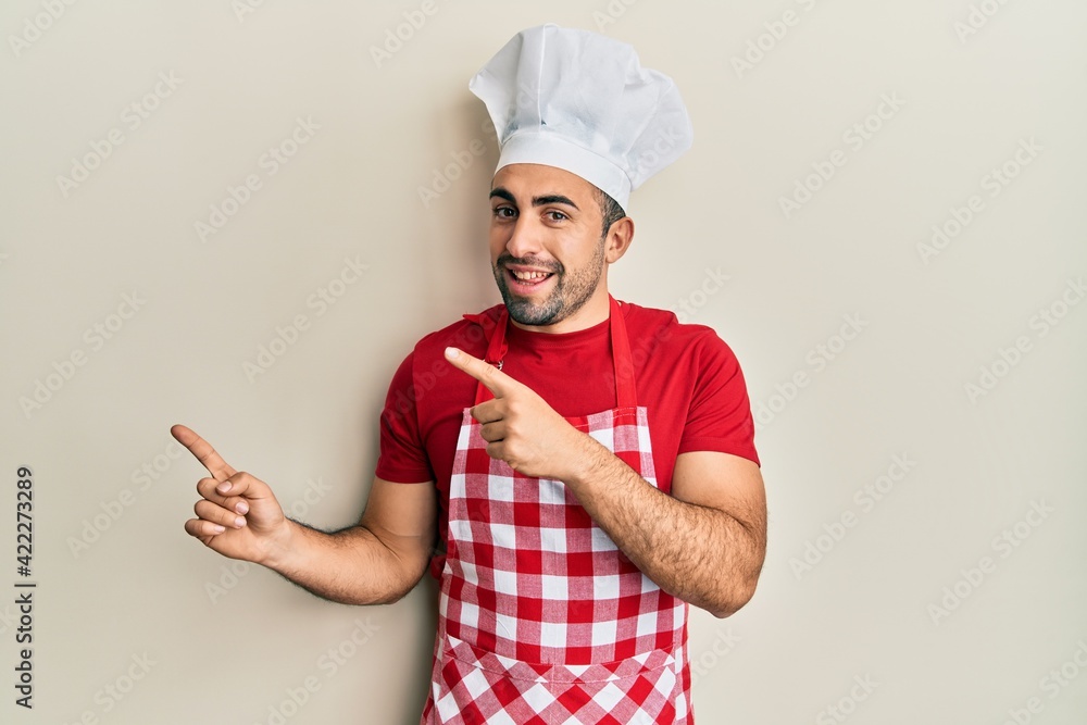 Young hispanic man wearing baker uniform smiling and looking at the camera pointing with two hands and fingers to the side. Young hispanic man wearing baker uniform smiling and looking at the camera pointing with two hands and fingers to the side.