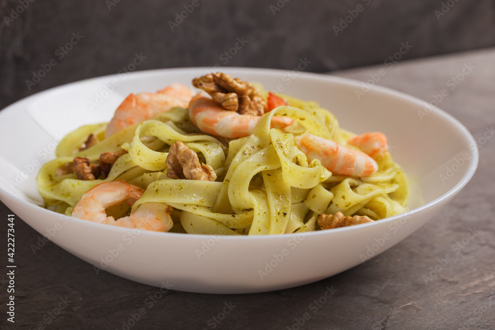 Pasta seafood. Close up of Tagliatelle with shrimps, pesto sauce, walnut on white plate ready to eat. Mediterranean cuisine.