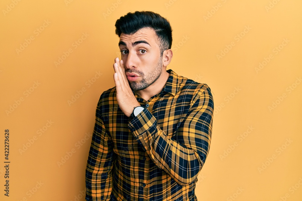 Fototapeta premium Young hispanic man wearing casual clothes hand on mouth telling secret rumor, whispering malicious talk conversation