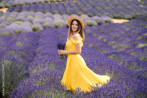Beautiful young woman portrait in lavender field. An attractive girl with long curly hair in a long dress is dreaming.