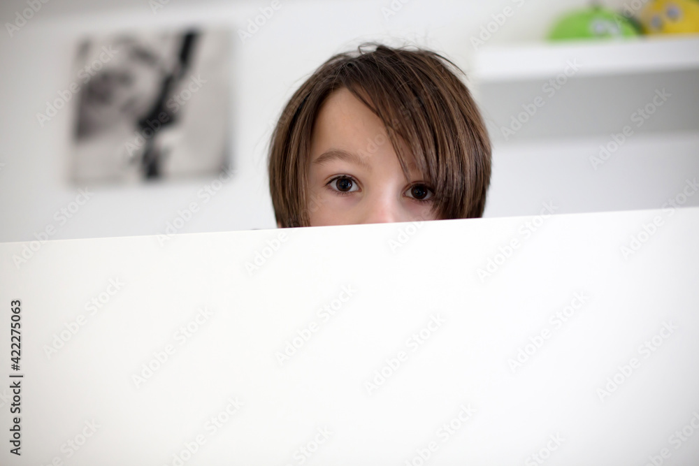 Cute child, hiding in bed, only eyes peeping out above the wooden board Cute child, hiding in bed, only eyes peeping out above the wooden board