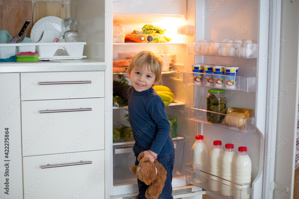 Cute toddler blond child, opening the fridge door and taking fruits adn vegetables and healthy food Cute toddler blond child, opening the fridge door and taking fruits adn vegetables and healthy food