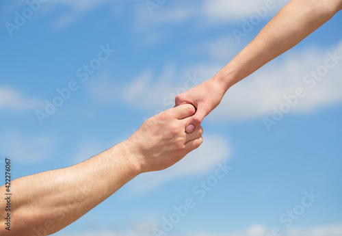 Lending a helping hand. Hands of man and woman reaching to each other, support. Solidarity, compassion, and charity, rescue. Giving a helping hand. Hands of man and woman on blue sky background © Yevhen