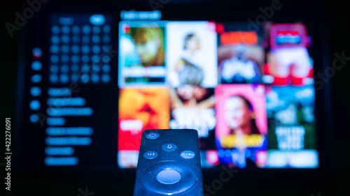 Isolated remote control browsing the tv shows on the television. Blurred shiny screen on the background.