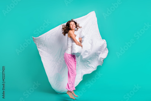 Full length photo of adorable pretty young lady nightwear jumping hugging pillow isolated teal color background photo