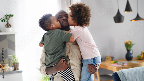 Foto Small children kissing father at home, multi ethnic family.