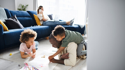 Multi ethnic family with two small children drawing pictures, home office.
