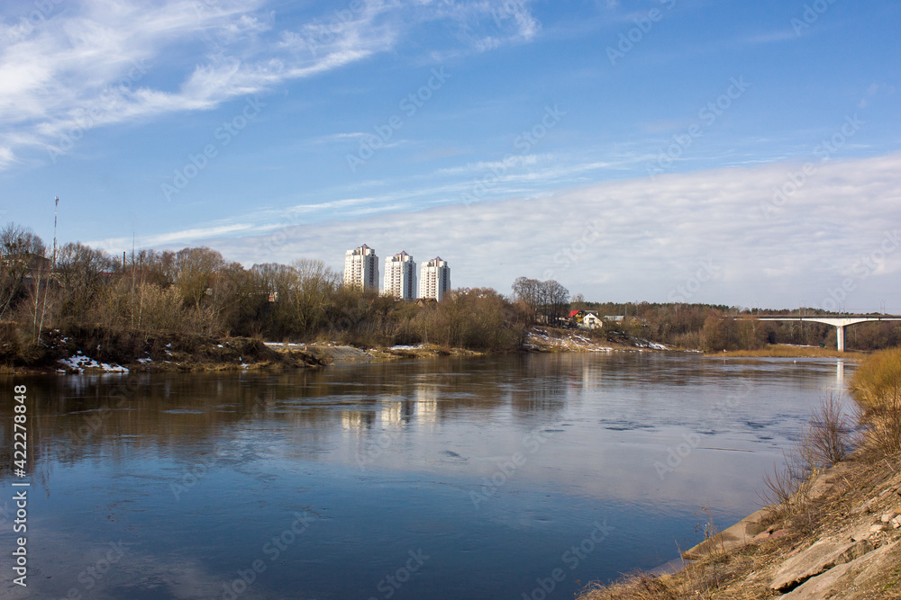 Grodno. Belarus. Spring landscape: blue sky, the Neman river and a bridge over the river in the distance, along the banks -  several high houses and old low houses.