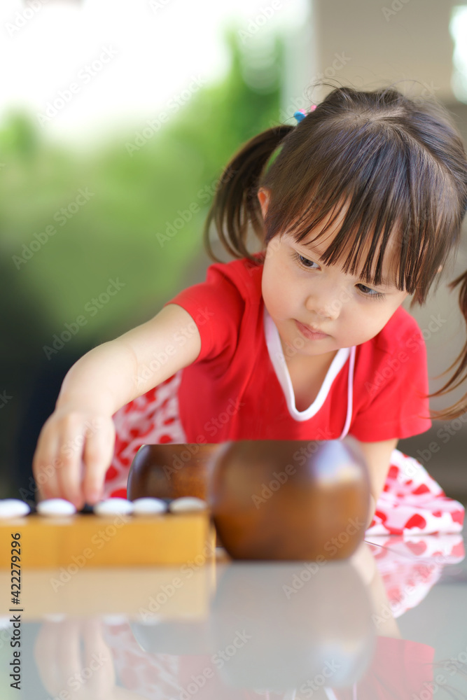 little cute asian girl playing black stone to the wooden baduk (GO) board game little cute asian girl playing black stone to the wooden baduk (GO) board game