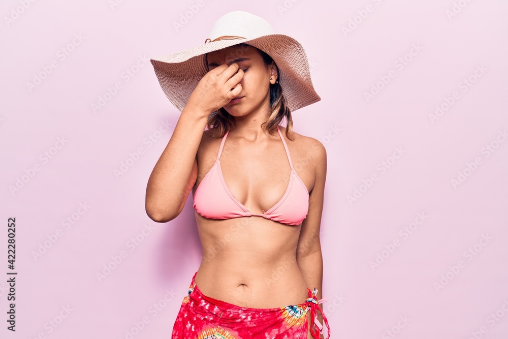 Young woman wearing bikini and hat tired rubbing nose and eyes feeling fatigue and headache. stress and frustration concept. Young woman wearing bikini and hat tired rubbing nose and eyes feeling fatigue and headache. stress and frustration concept.
