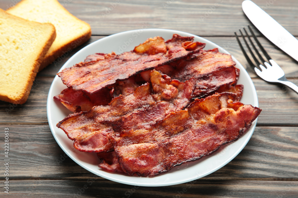Bacon fried slices in plate on brown background. Top view