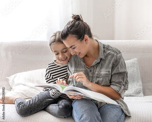 Young mom and daughter have fun together, doing homework with a book and a phone. photo