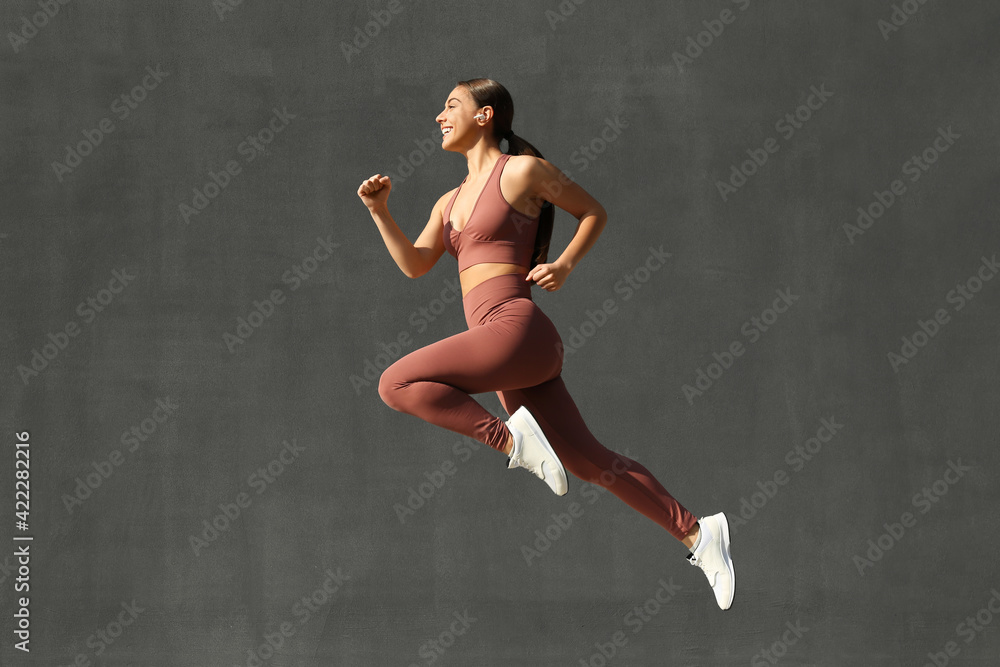 Young woman in stylish sports wear jumping on grey background