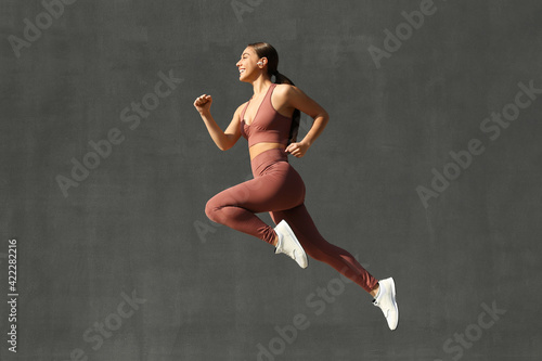 Young woman in stylish sports wear jumping on grey background