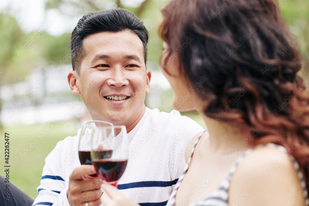 Portrait of smiling handsome young Asina man enjoying picnic with girlfriend and drinking wine Portrait of smiling handsome young Asina man enjoying picnic with girlfriend and drinking wine