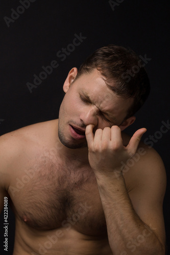 Man picks his nose on a black background. Muscular and athletic. Portrait of a man. Male model in studio