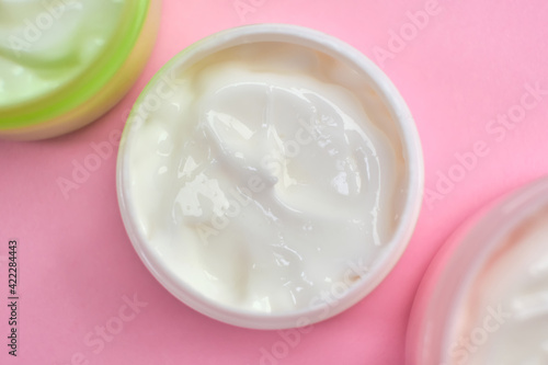 face cream in open multi-colored jars on pink background