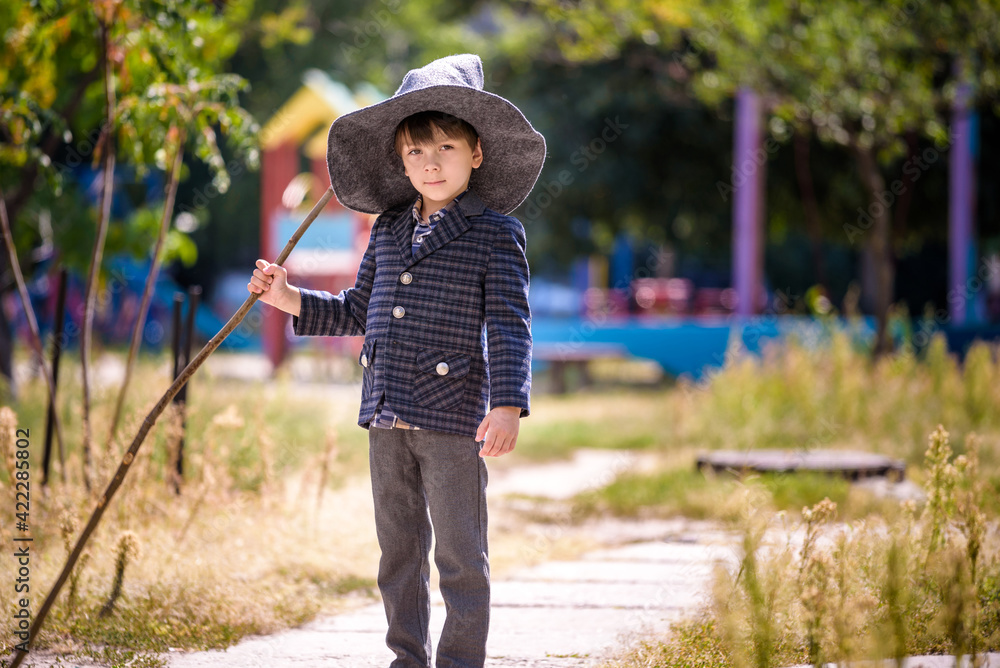 Toddler boy in pointed hat playing with magic wand outdoors. Little wizard. Halloween concept