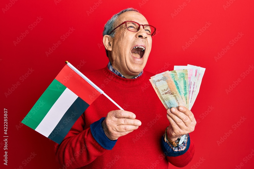 Handsome senior man with grey hair holding united arab emirates dirham banknotes angry and mad screaming frustrated and furious, shouting with anger looking up. Handsome senior man with grey hair holding united arab emirates dirham banknotes angry and mad screaming frustrated and furious, shouting with anger looking up.