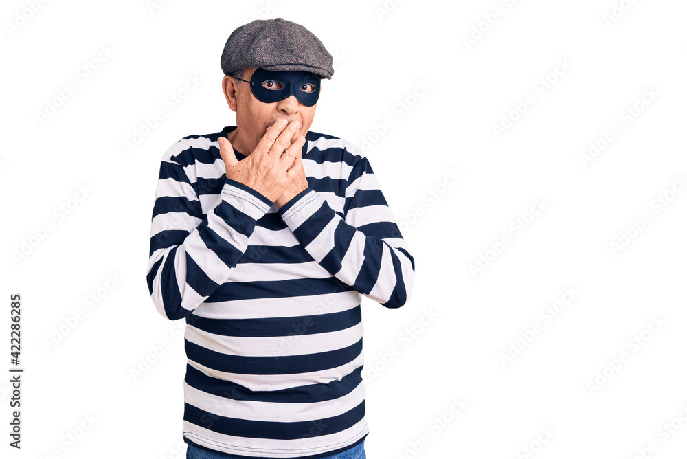 Senior handsome man wearing burglar mask and t-shirt laughing and embarrassed giggle covering mouth with hands, gossip and scandal concept Senior handsome man wearing burglar mask and t-shirt laughing and embarrassed giggle covering mouth with hands, gossip and scandal concept