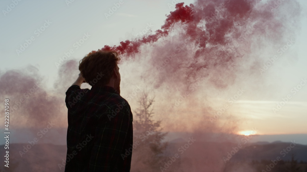Guy dancing in mountains at sunset. Excited guy holding active smoke grenade 