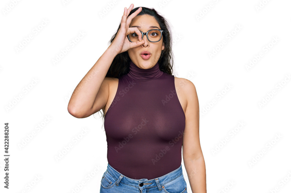 Brunette young woman wearing casual clothes and glasses doing ok gesture shocked with surprised face, eye looking through fingers. unbelieving expression. Brunette young woman wearing casual clothes and glasses doing ok gesture shocked with surprised face, eye looking through fingers. unbelieving expression.