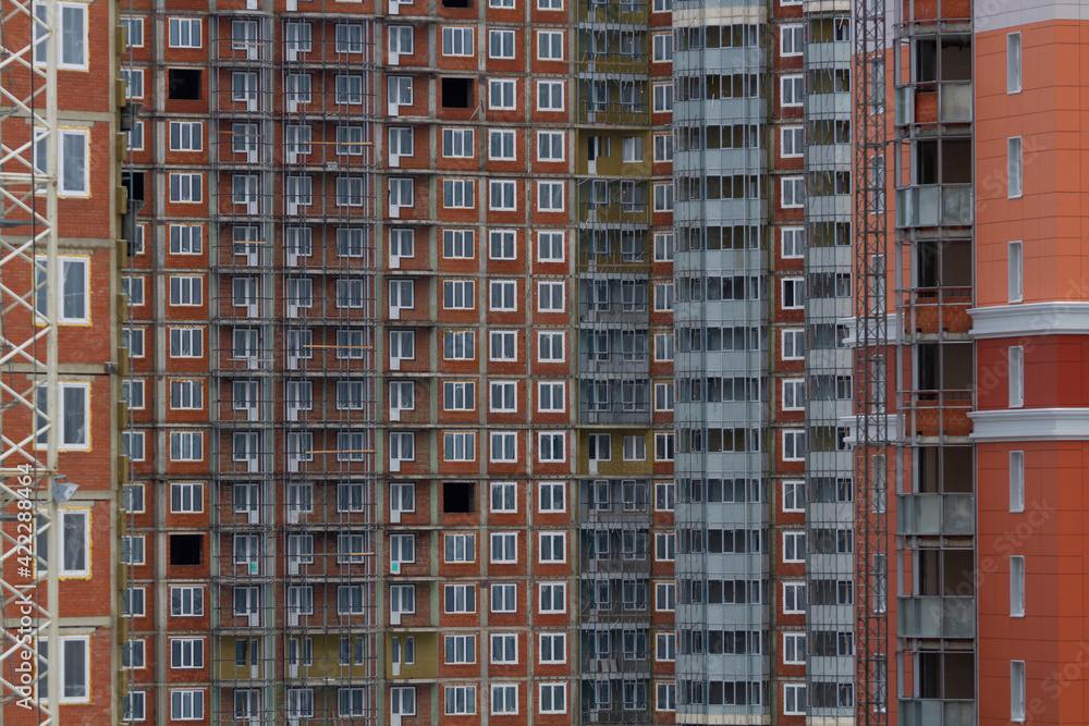 Fototapeta premium Construction of a residential multi-storey building. Windows, balconies. Concrete, brick walls. Blue, white, brown colors.