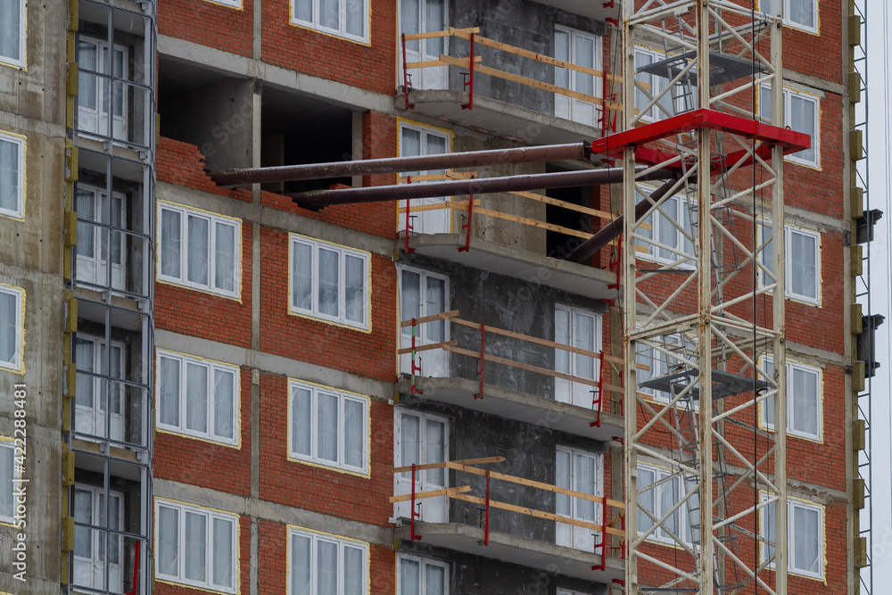Fototapeta premium Fastening the crane support to the house. Construction of a residential multi-storey building. Windows, balconies. Concrete, brick walls.