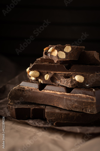 Dark chocolate with almonds and hazelnuts in a stack on brown background