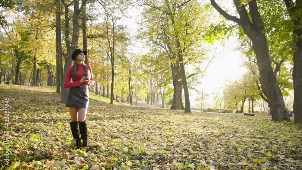 Stylish girl posing with smile and drinking a cup of tea in sunny autumn park Stylish girl posing with smile and drinking a cup of tea in sunny autumn park