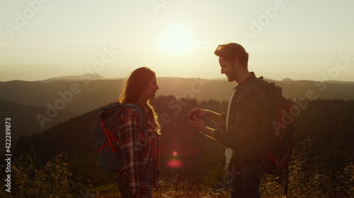 Hikers enjoying hike in mountains at sunset. Man proposing marriage to woman 