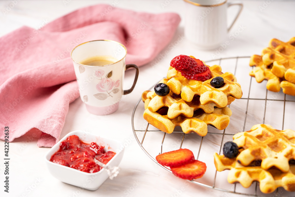 Delicious breakfast table, waffles with berries, jam and cup of coffee. Front view. Marble background. Selective focus. 