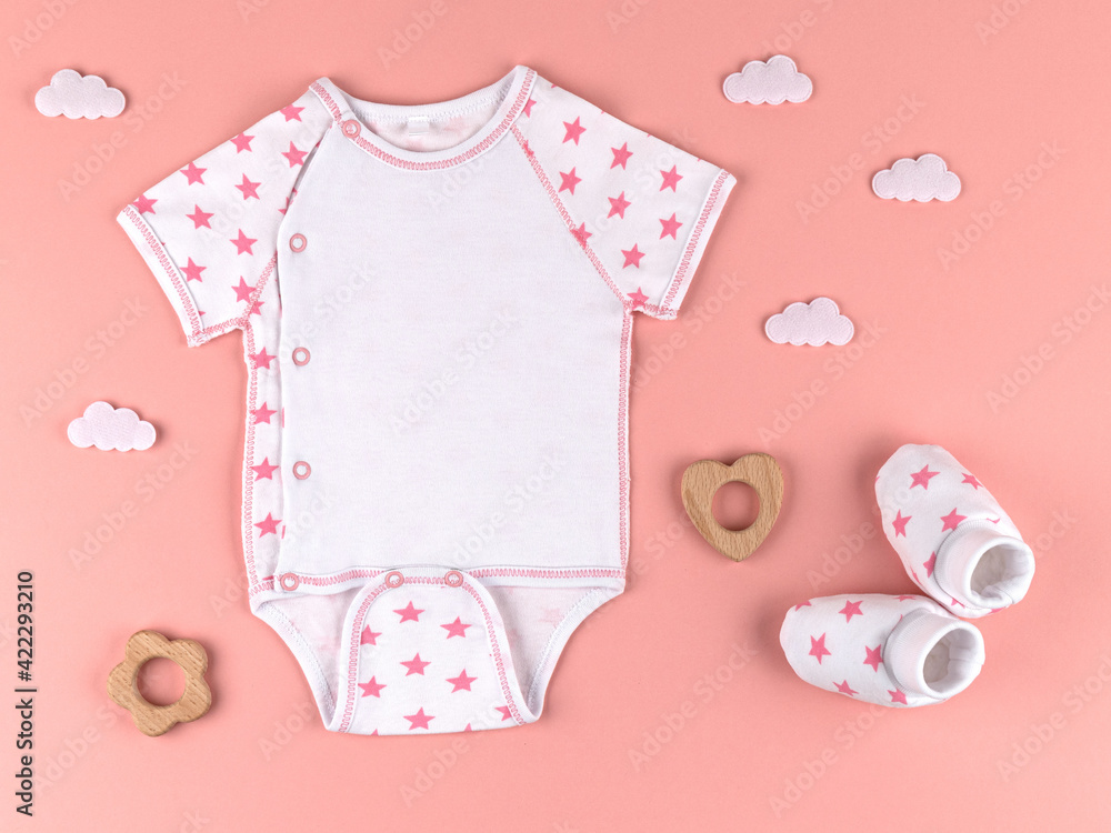 Bodysuit and booties for a newborn boy in the clouds and a wooden toys for the newborn on a pink background. We're expecting a girl. It's time to give birth. Newborn clothes and accessories. Flat lay